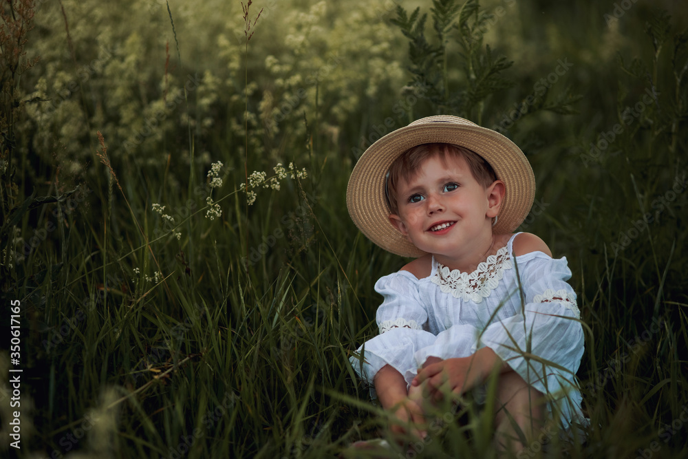  Cute little girl in a white dress and hat in the field at sunset time