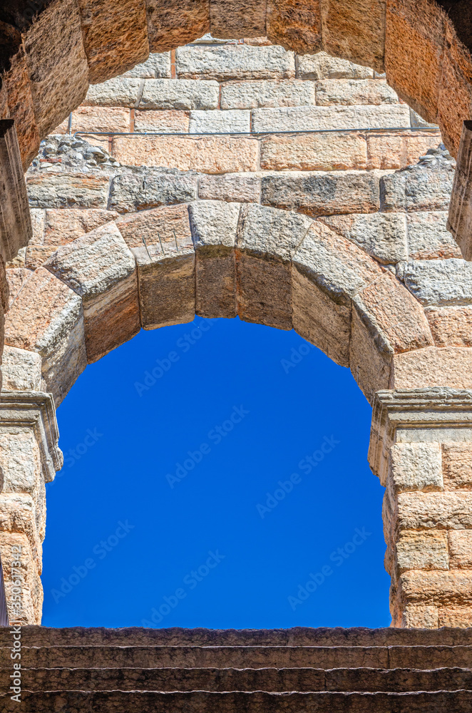 Blue clear sky through limestone brick arch window of The Verona Arena, Roman amphitheatre Arena di Verona ancient building, Verona city historical centre, staircase foreground, Veneto Region, Italy