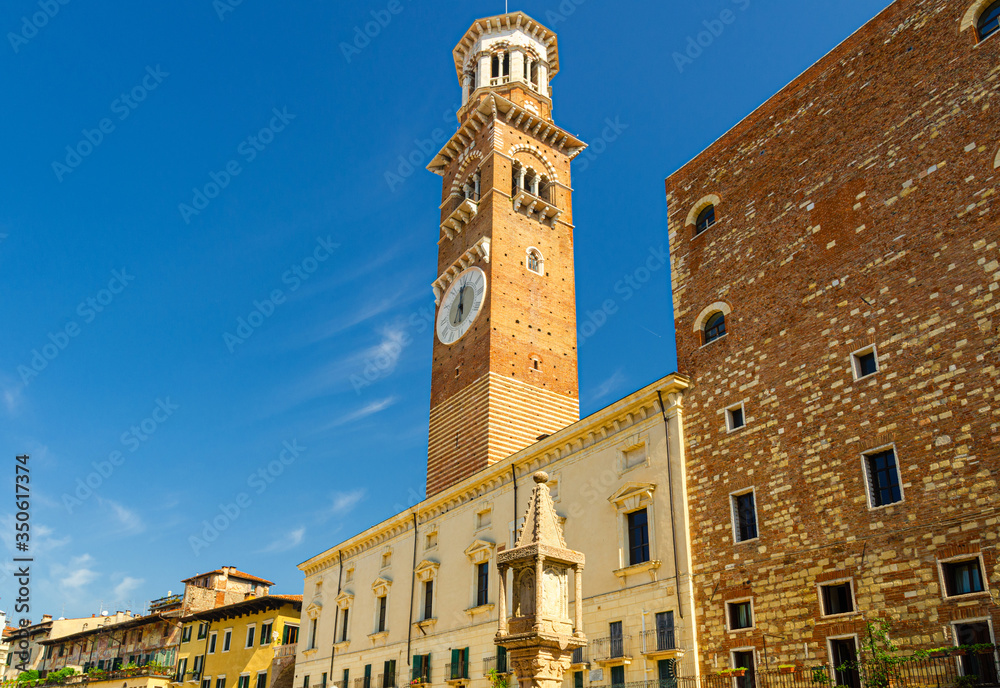 Torre dei Lamberti clock tower of Palazzo della Ragione palace building in Piazza Delle Erbe square in Verona city historical centre, blue sky background, Veneto Region, Northern Italy