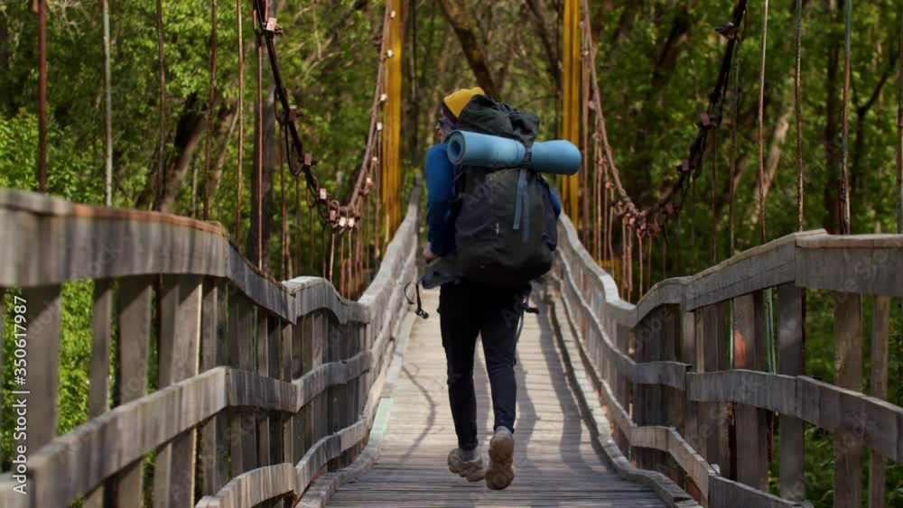 Young man with big backpack running on the bridge in the forest Young man with big backpack running on the bridge in the forest