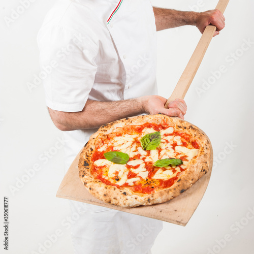 italian pizza margherita with mozzarella cheese, tomatoes, basilico resting on the pizza maker wooden shovel, from the top, white background