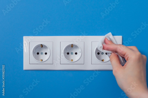 Woman cleaning electrical european outlet, socket with disinfectant wet wipe - close up view. Disinfection, protection, prevention, housework, COVID-19, coronavirus safety and sanitation concept