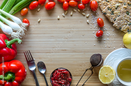 Cherry tomatoes, onions, fitness bread, pine nuts, tea, lemon, jam, arranged in a circle on a bamboo sheet. Healthy breakfast ingredients on the table. Kitchen composition before cooking, preparation.