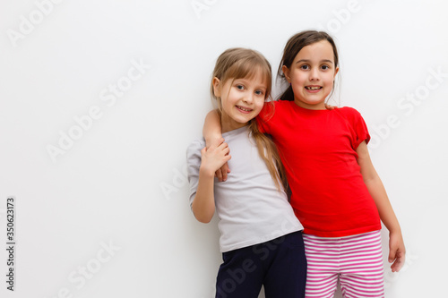 Cute little caucasian girls are keeping hands up, looking at camera and smiling, isolated on a white background