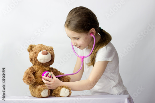 Beautiful little girl pretending to be a nurse or doctor and auscultate and measure the temperature her teddy-bear