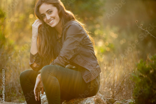 Girl with brown hair sitting on a stone smiling