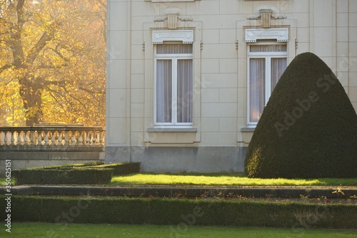 Facade of the Den Brandt Castle in Nachtegalen park, Antwerp, Belgium. Beautiful green garden. Tall golden trees in the background. Fairy autumn scene. National landmark, sightseeing theme