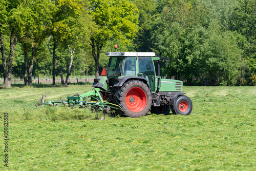 Green tractor mowing tall green grass in early spring in the Netherlands.