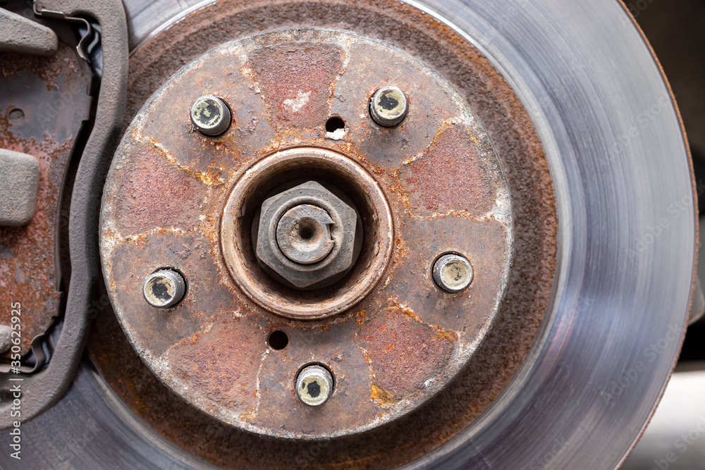 Rusty back car wheel hub with five bolts and brake disc at tire shop. Car without a wheel while replacing on the tire service center. Closeup view Rusty back car wheel hub with five bolts and brake disc at tire shop. Car without a wheel while replacing on the tire service center. Closeup view