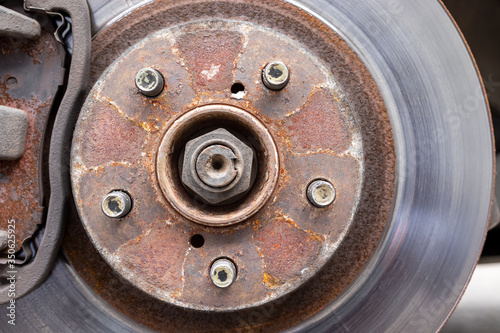 Rusty back car wheel hub with five bolts and brake disc at tire shop. Car without a wheel while replacing on the tire service center. Closeup view