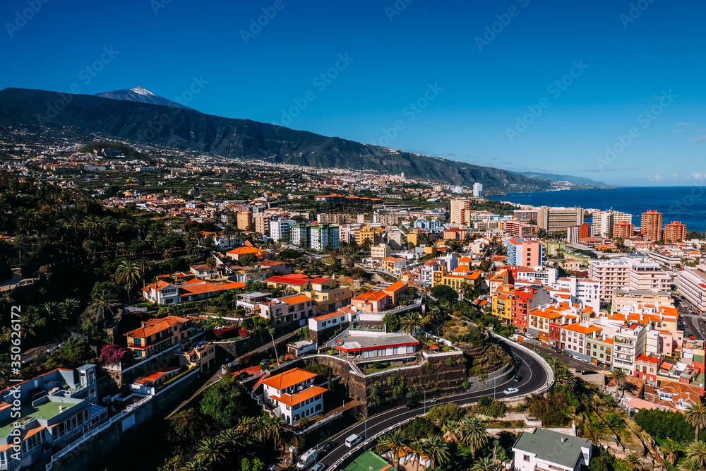 Landscape of the city of Puerto de La Cruz and the Teide volcano on a Sunny day under a blue sky. Tropical island with a volcano near the city