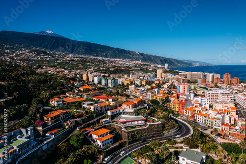 Landscape of the city of Puerto de La Cruz and the Teide volcano on a Sunny day under a blue sky. Tropical island with a volcano near the city