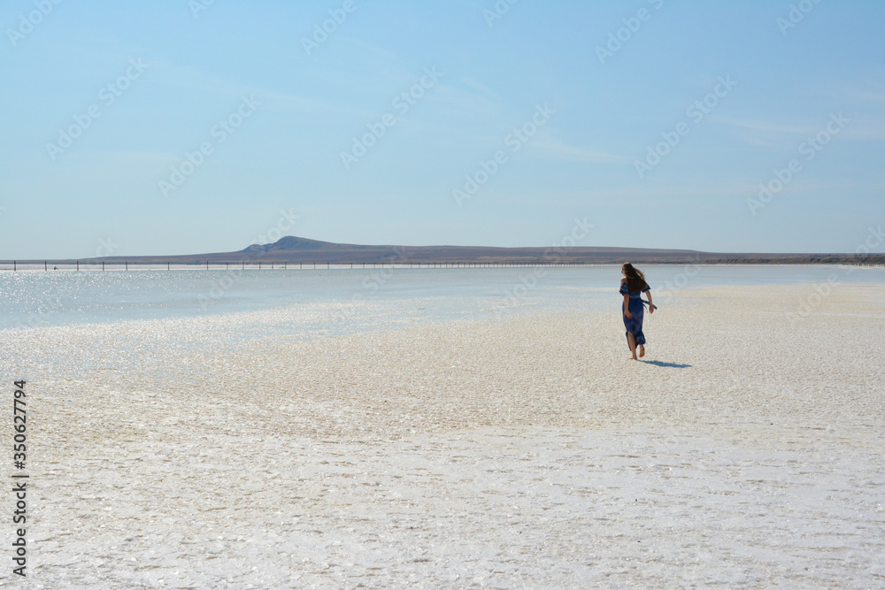 Salt lake Baskunchak, Astrakhan region, Russia. A girl in a blue dress is walking along a salt lake.