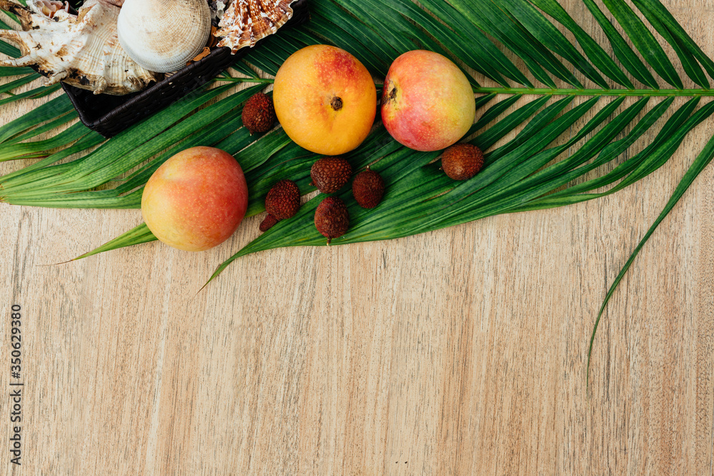 Flat lay, top view, Mix of Exotic fruits and palm leaf on a brown background: pineapples, mangoes, mangosteen, lychee, citrus fruits