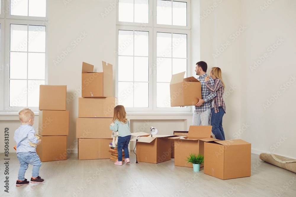 Happy family with children moving with boxes in a new apartment house.