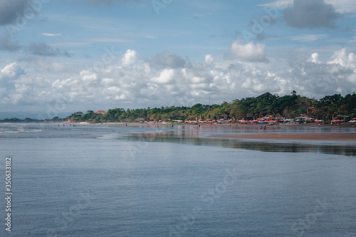 Tropical seascape: view of the ocean waves and the beach with tourists relaxing. © Evgenii Starkov