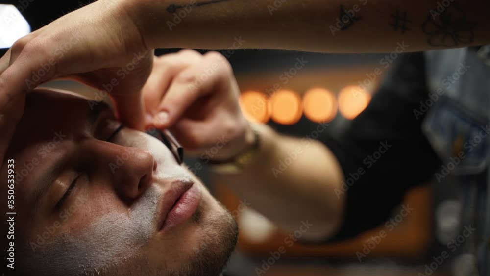 Professional barber shaves customer beard with straight razor. Beard cut with old-fashioned blade at barbershop. Handsome macho man getting his beard shaved in studio. Close-up shot. Professional barber shaves customer beard with straight razor. Beard cut with old-fashioned blade at barbershop. Handsome macho man getting his beard shaved in studio. Close-up shot.