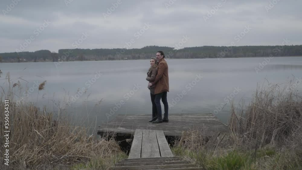 Extreme wide shot of hugging Caucasian man and woman standing on pier, talking and smiling. Side view of happy couple dating outdoors. Leisure, love, togetherness, lifestyle. Extreme wide shot of hugging Caucasian man and woman standing on pier, talking and smiling. Side view of happy couple dating outdoors. Leisure, love, togetherness, lifestyle.