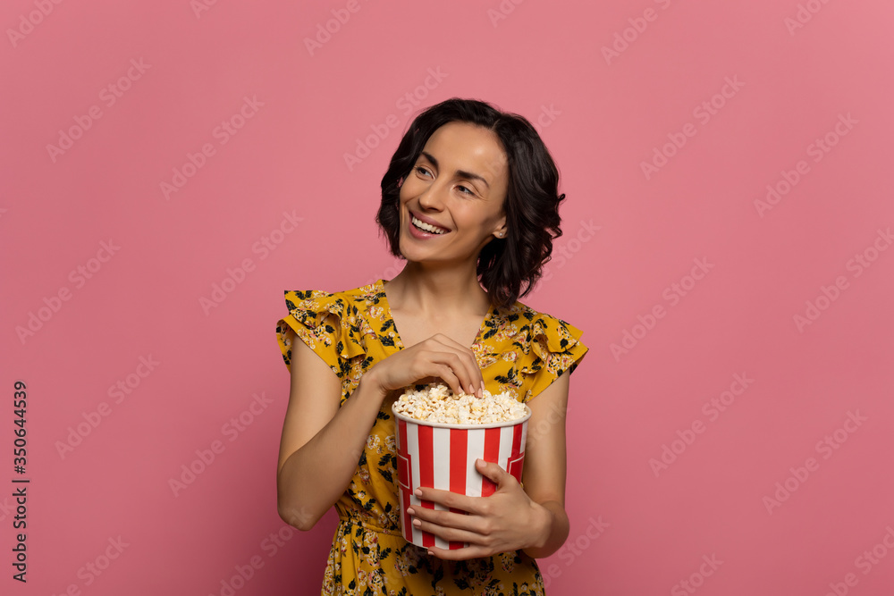 Popcorn lover. Close-up photo of a young smiling lady, who is eating popcorn, smiling and looking to the left.