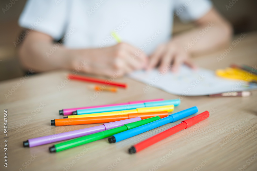 The child at the table draws on a blank sheet, around many colored pencils and felt-tip pens. Close-up of pencils. The child at the table draws on a blank sheet, around many colored pencils and felt-tip pens. Close-up of pencils.