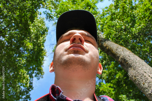 Man's face in a cap from below under the chin against the background of green trees and blue sky photo