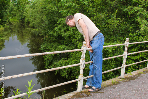 Man in jeans on bridge looking down to the water against of green trees background