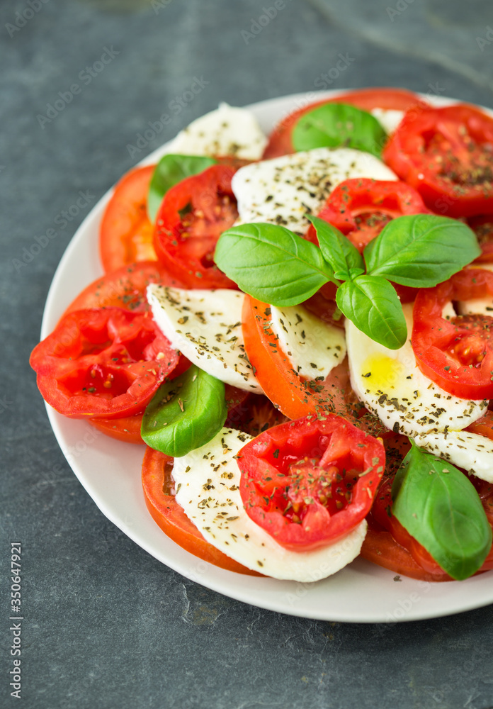 Fresh caprese salad with mozzarella, tomato, basil and spices on the plate