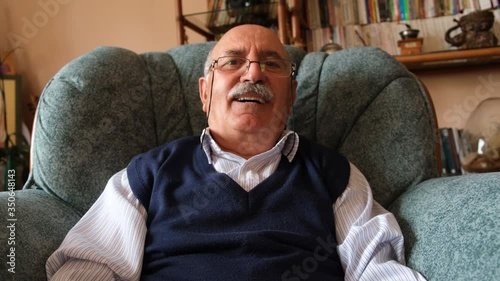 Smiling senior man look at camera and talk make live video conference call. Making online chat by using phone and  sit on sofa at home, 4K close up video chat concept