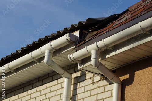 long plastic white gutter pipes on the wall of the house under the roof