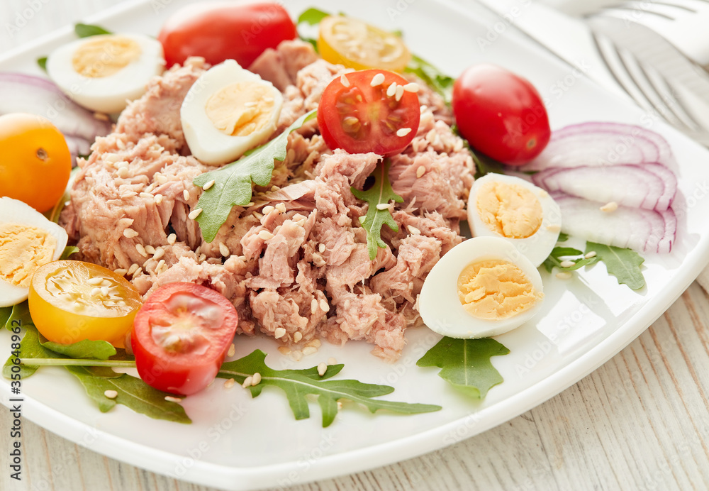 Tuna salad with arugula and tomatoes on light wooden background. Healthy food, seafood menu, Tuna salad with arugula and tomatoes on light wooden background. Healthy food, seafood menu,