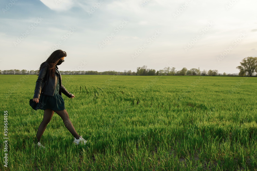 A girl in a medical mask runs or walks on a green field. Quarantine spring summer. coronavirus. COVID 19. Flu virus, colds A girl in a medical mask runs or walks on a green field. Quarantine spring summer. coronavirus. COVID 19. Flu virus, colds