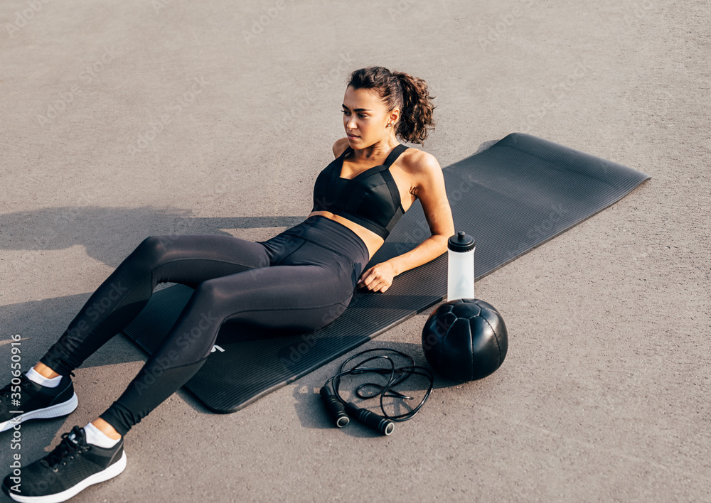 Female in sportswear lying on an exercise mat with a medicine ball, skipping rope and bottle