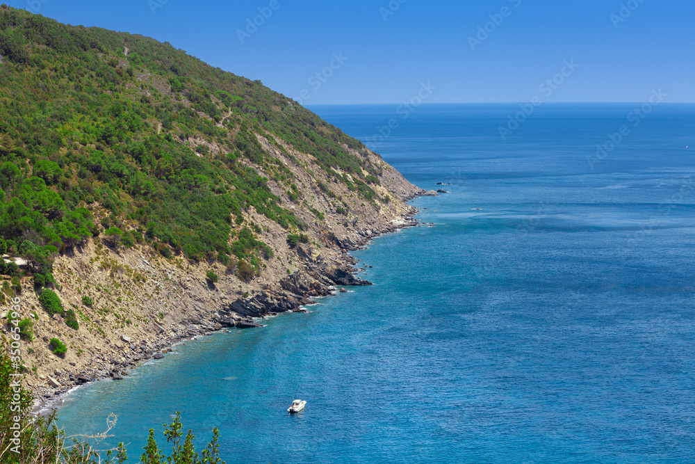 Coastline with cliff mountain and seashore view. Pitched rock face on the sea. Elba island in Italy. Aerial view with rocks and boat. Green vegetation and blue sky.