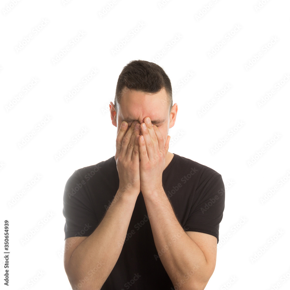 Man in t-shirt covering his face with hands over white background. Man in t-shirt covering his face with hands over white background.