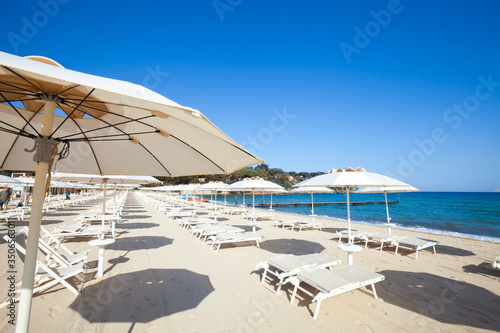 Fototapeta Naklejka Na Ścianę i Meble -  Beach and Italian Tyrrhenian coast with a multitude seamsless of beach umbrellas, deckchairs for vacationers. Trees and nature in the background.