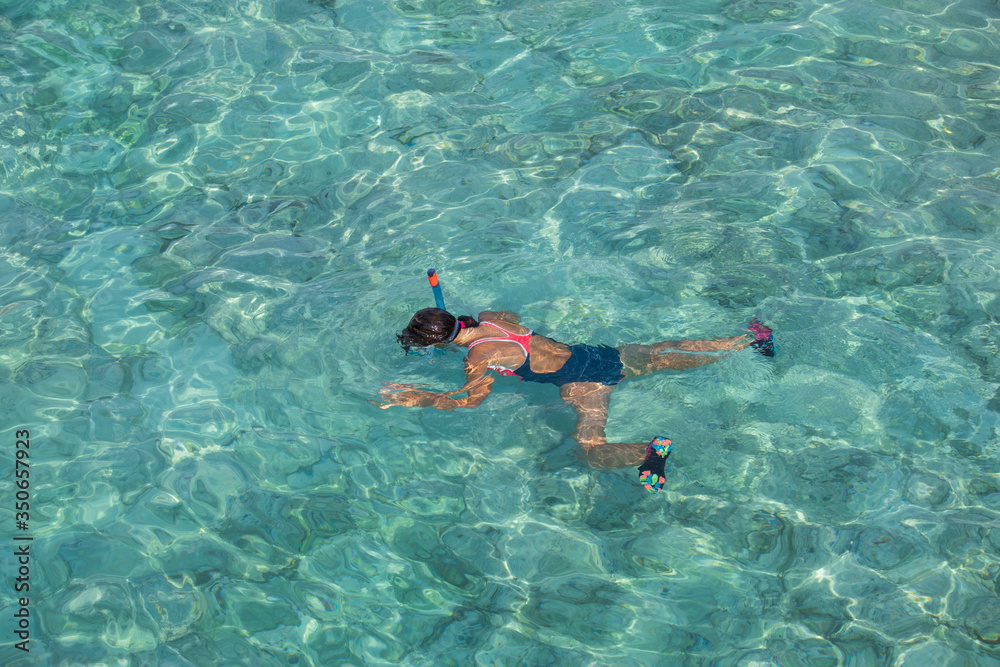 A girl in a diving mask swims in clear water on her stomach. The view from the top.