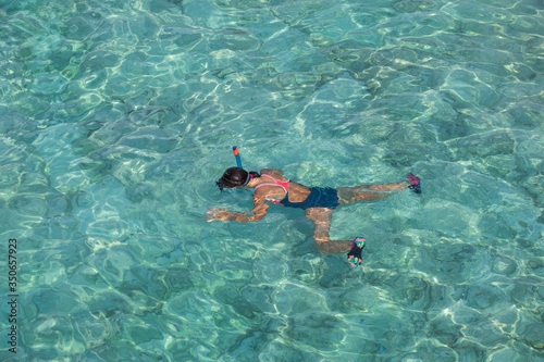 A girl in a diving mask swims in clear water on her stomach. The view from the top. © dadoodas