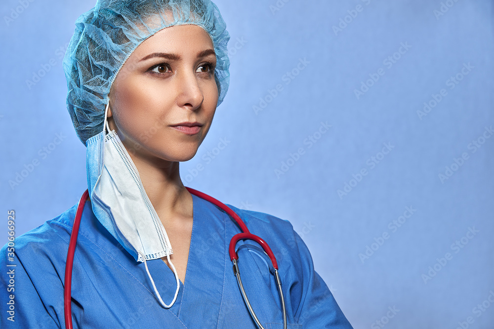 Portrait of a doctor in medical uniform, protective mask, surgical cap, with stethoscope isolated on blue background. Coronavirus Epidemic COVID-19, space for text