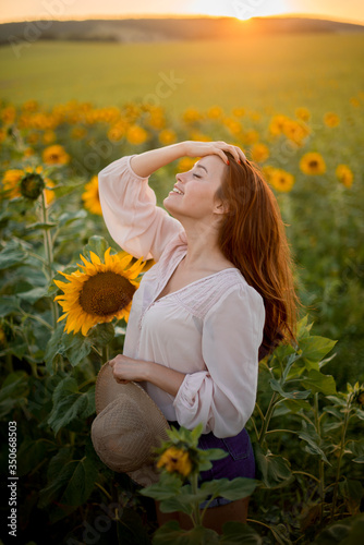 Konstfotografi Beautiful red-haired girl with gray eyes walks in a summer sunflower field