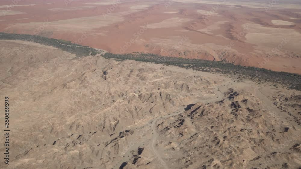 Aerial shot of rocky barren landscape on sunny day, scenic view of trees and plants in desert seen from airplane - Sossusvlei, Namibia Aerial shot of rocky barren landscape on sunny day, scenic view of trees and plants in desert seen from airplane - Sossusvlei, Namibia