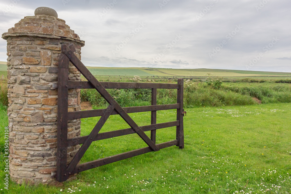 Open wooden gate into farmers green field.  Old stone pillar. Kirkwall Orkney Scotland