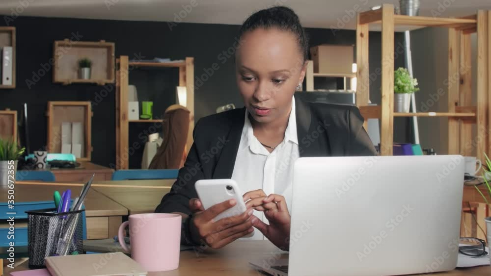 Young african american woman using phone looking at screen surfing social media at office Young african american woman using phone looking at screen surfing social media at office