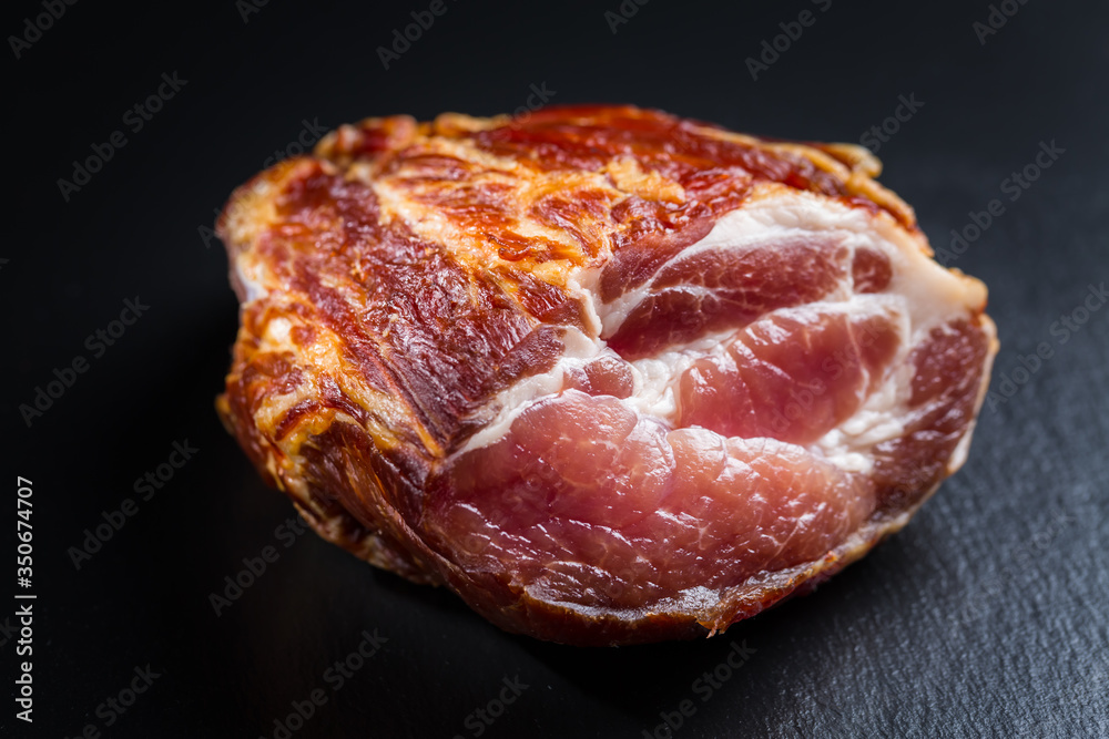 Piece of smoked ham with pepper and herbs on black background