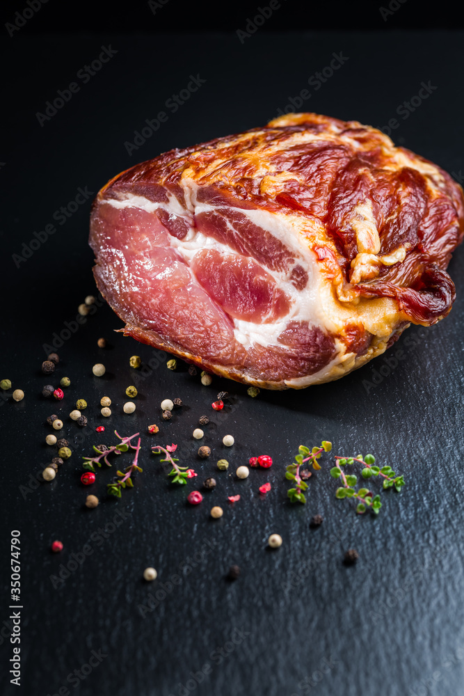 Obraz premium Piece of smoked ham with pepper and herbs on black background