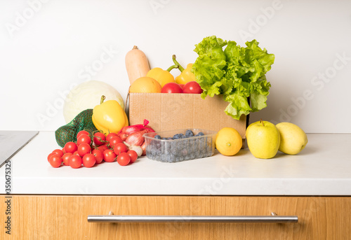 Fototapeta Naklejka Na Ścianę i Meble -  groceries box with vegetables and fruits on white kitchen background. Food delivery services during coronavirus pandemic and social distancing. Shopping online.