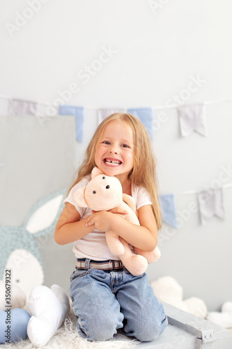happy smiling toothless little blonde girl. Child smiling withouth his milk teeth in children room. Sweet little redhead girl is hugging a teddy bear on at home. child plays with a toy in kindergarten photo