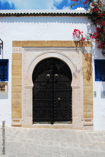 Traditional Tunisian black metal door with a pattern on a white wall with stone platbands. Sidi Bou Said, Tunisia