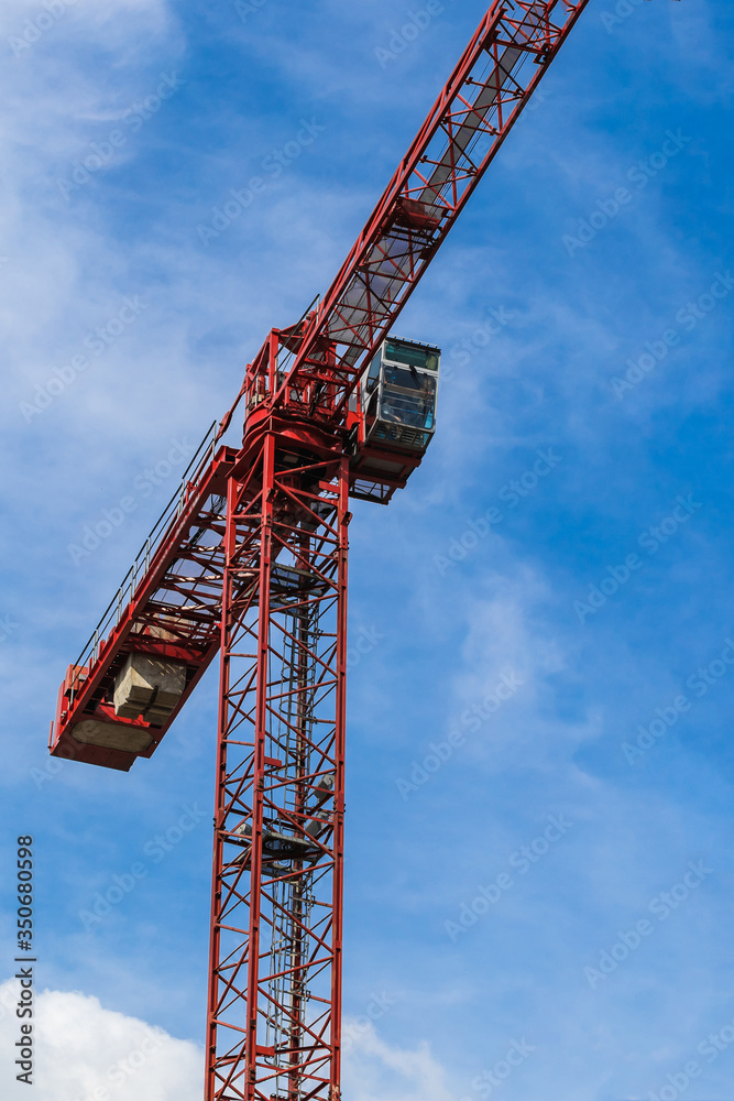 Red tower crane against blue sky with white clouds. Close up. Vertical photo. Copy space. Red tower crane against blue sky with white clouds. Close up. Vertical photo. Copy space.