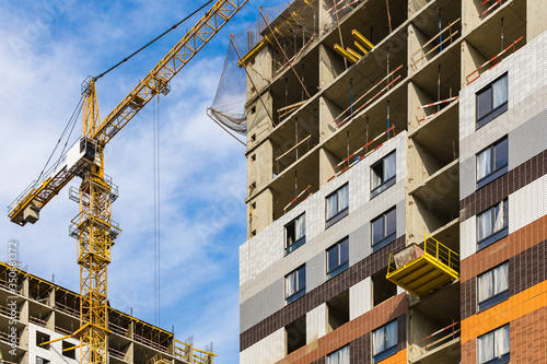 One yellow high crane against a house and sky during the construction phase. Industry concept for low-income young families. Mortgage, business, real estate loan. Summer. Daytime.