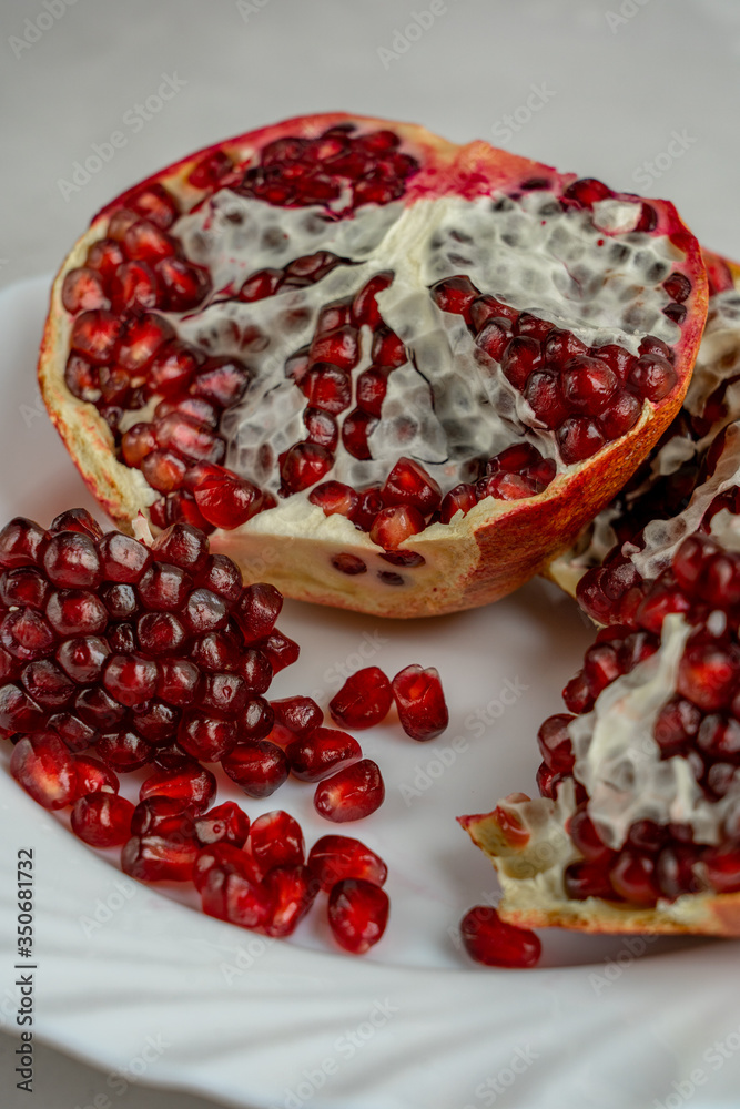 Half of ripe juicy pomegranate and pomegranate seeds are laying on white plate Half of ripe juicy pomegranate and pomegranate seeds are laying on white plate